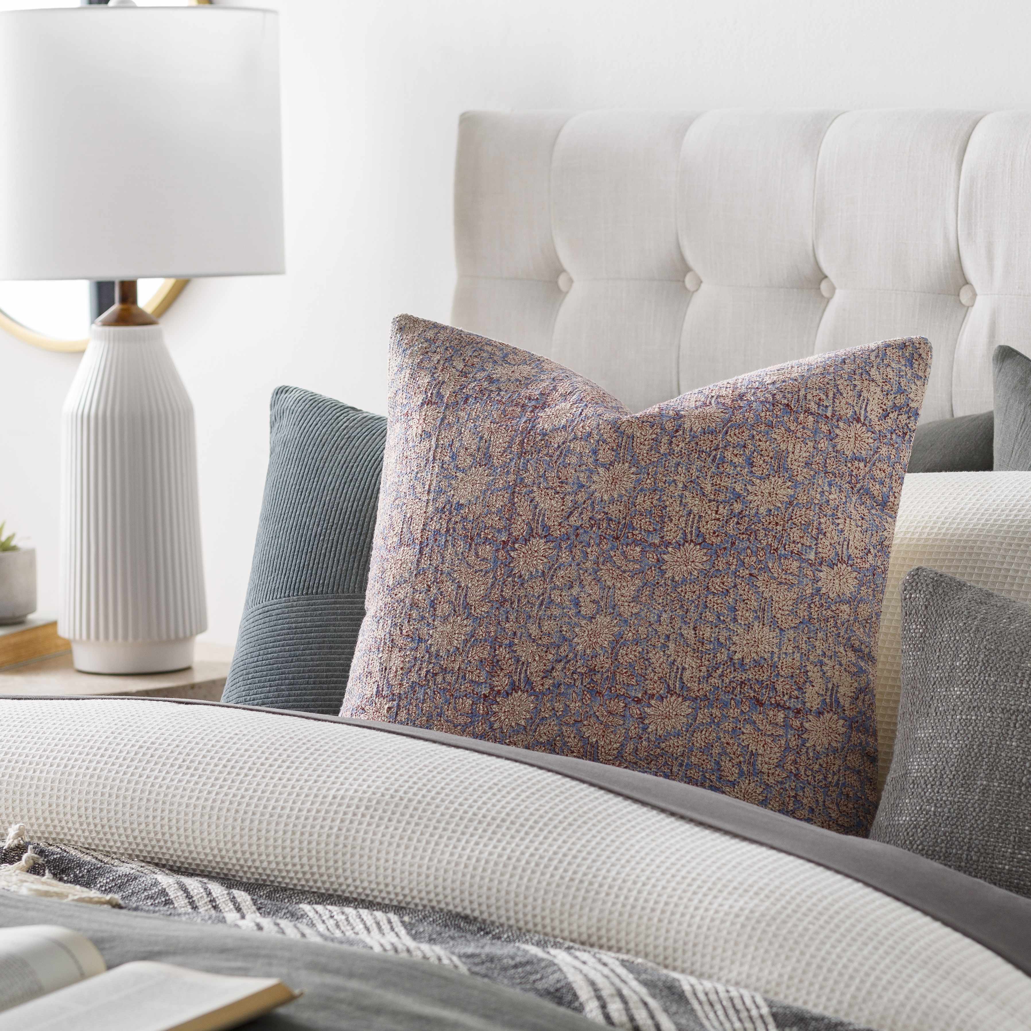 Decorative pillows on a bed with a lamp in the background