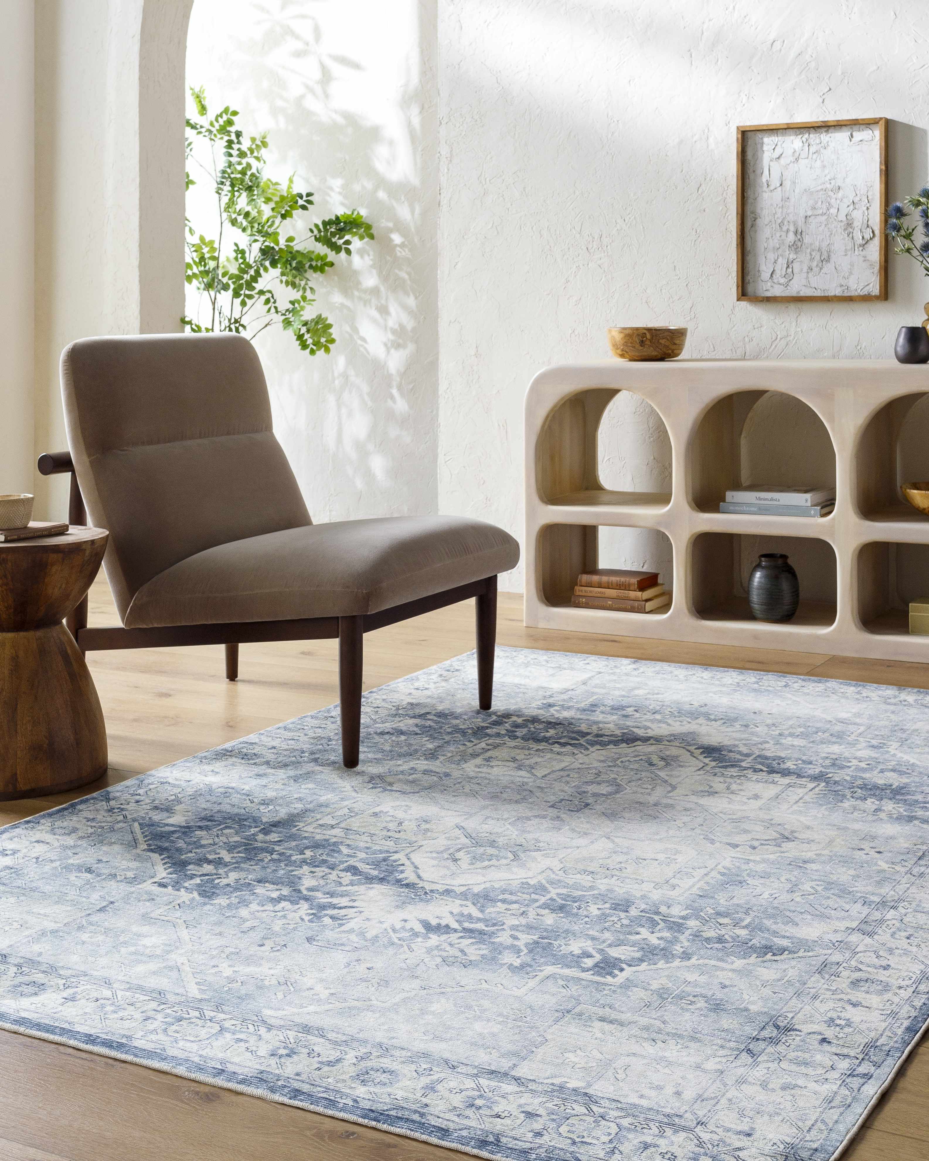 Living room with a blue and white patterned rug, beige armchair, and wooden side table.