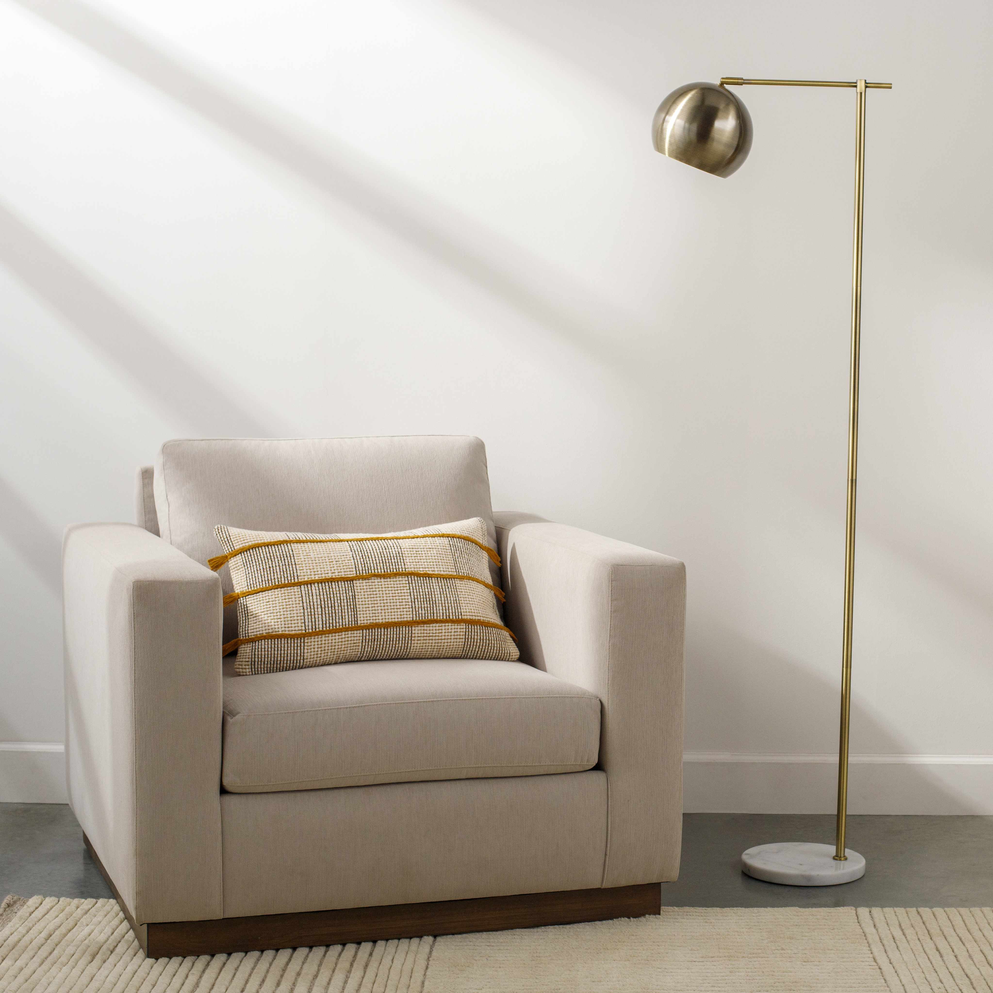 Beige armchair with a striped pillow next to a gold floor lamp in a room with white walls.