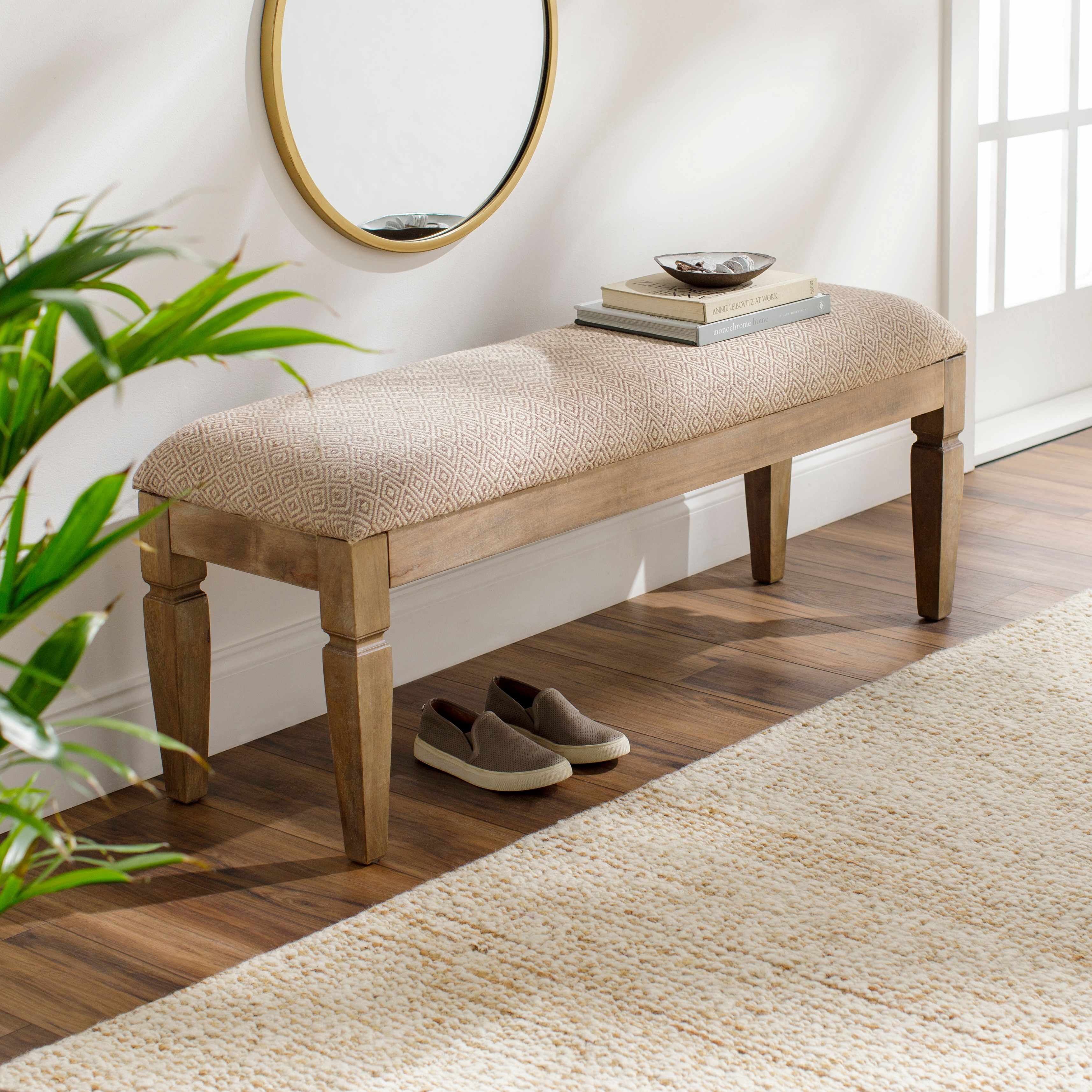 Wooden bench with textured cushion in a room with a mirror, books, and shoes.