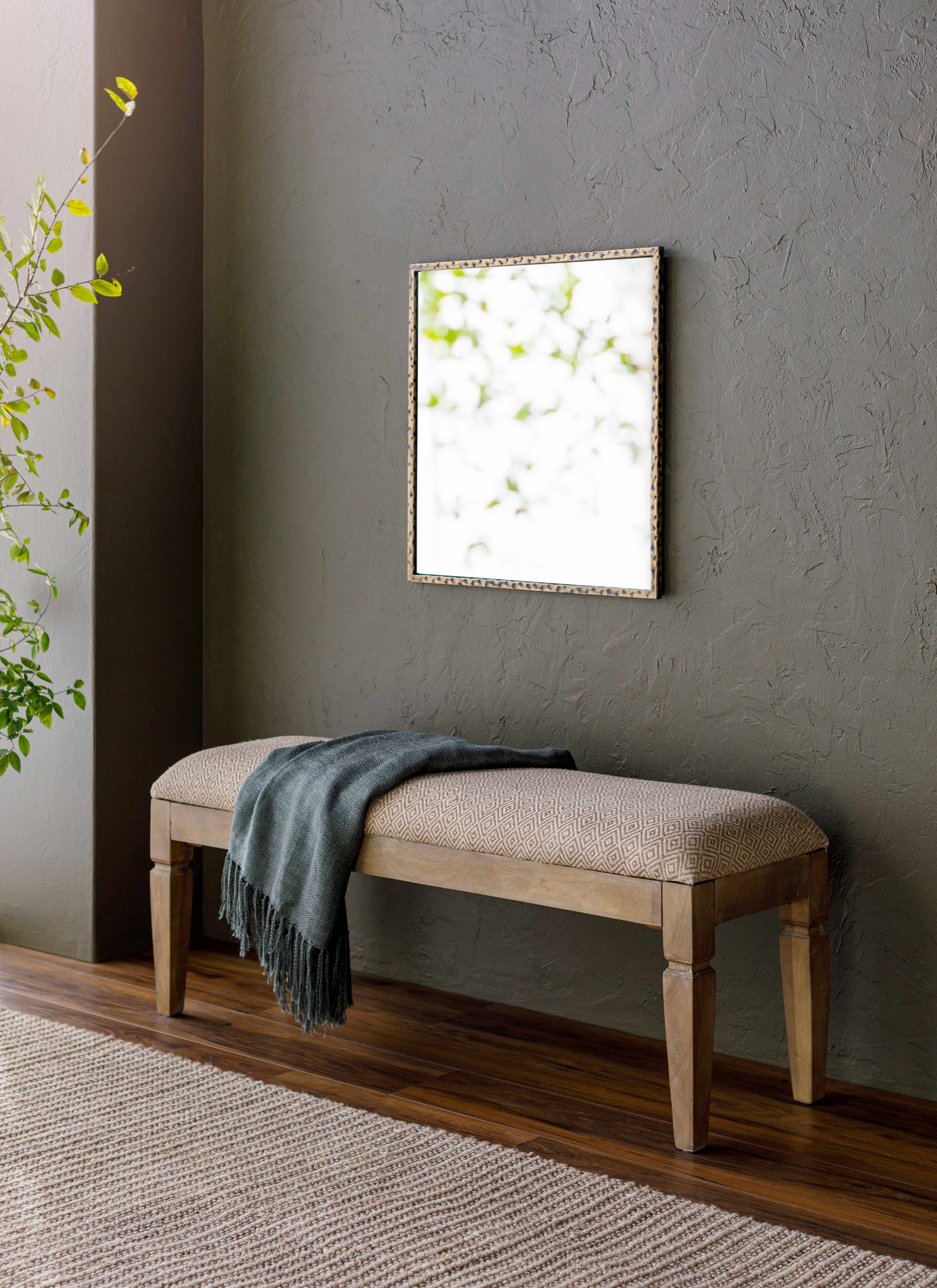 Beige bench with a green blanket against a gray wall with a framed picture