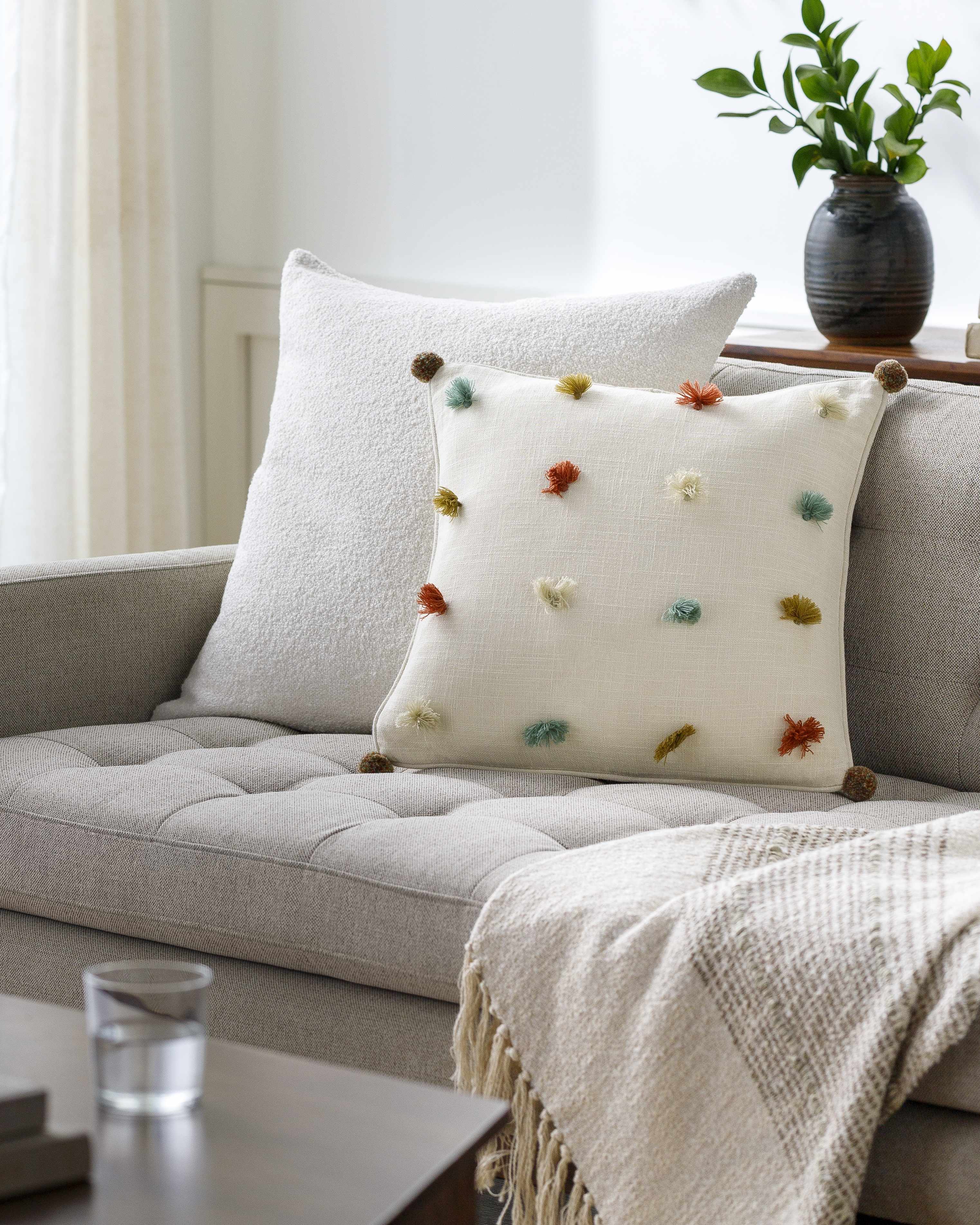 Decorative pillow with colorful pom-poms on a gray sofa in a living room setting.