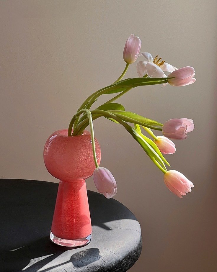 Pink vase with tulips on a dark surface against a beige background
