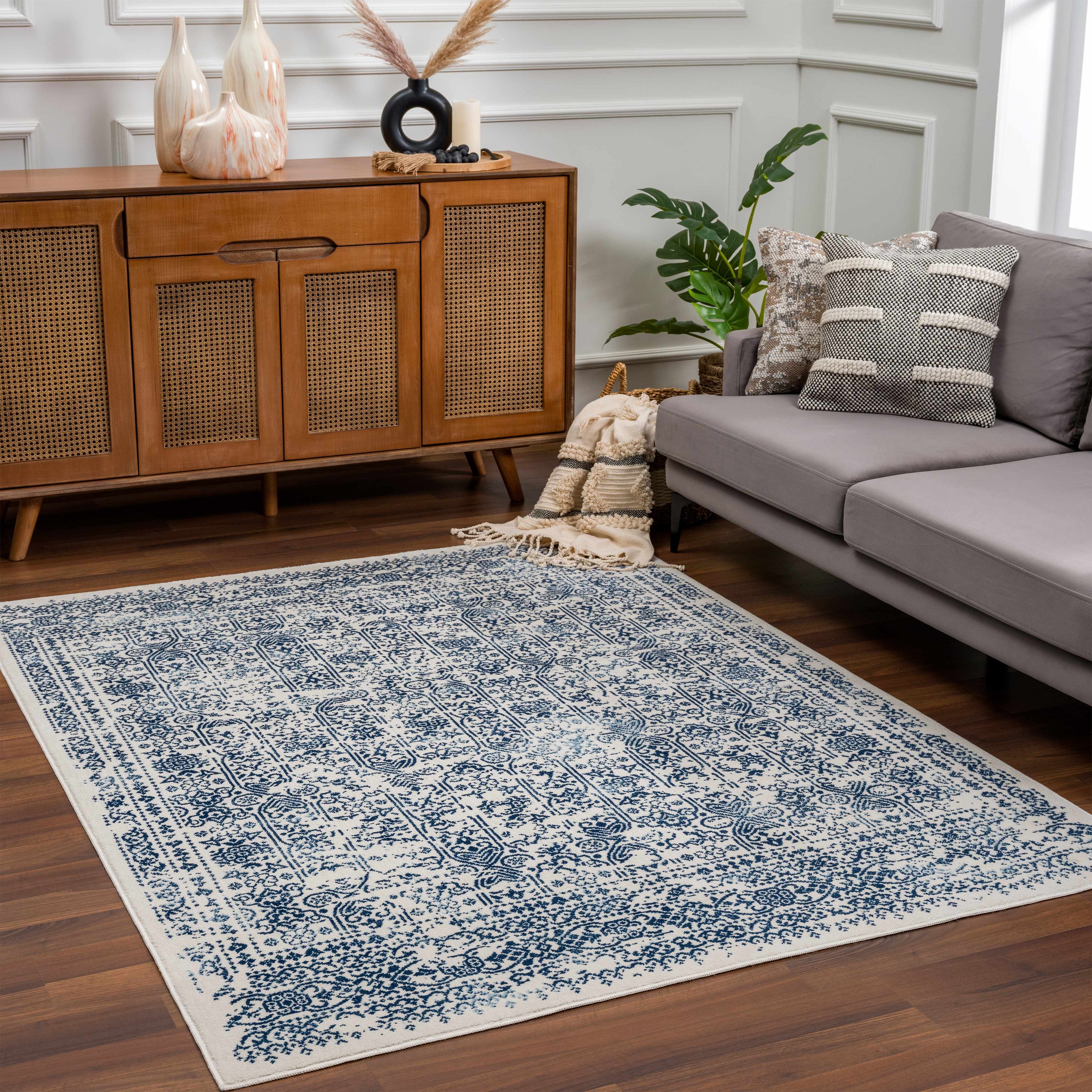 Living room with a blue and white patterned rug, gray sofa, wooden cabinet, and decorative items.