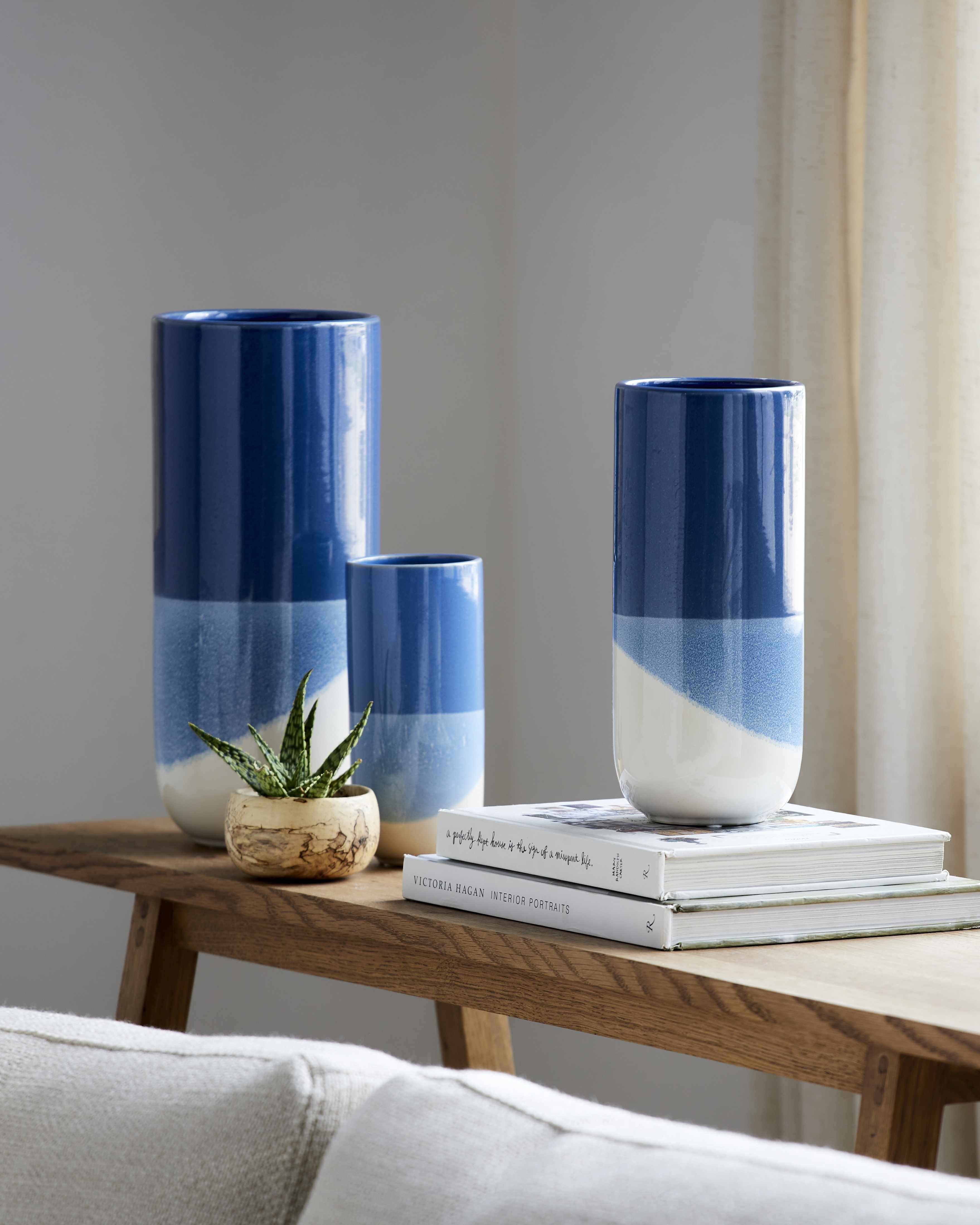 Three blue and white vases on a wooden table with books and a small plant.