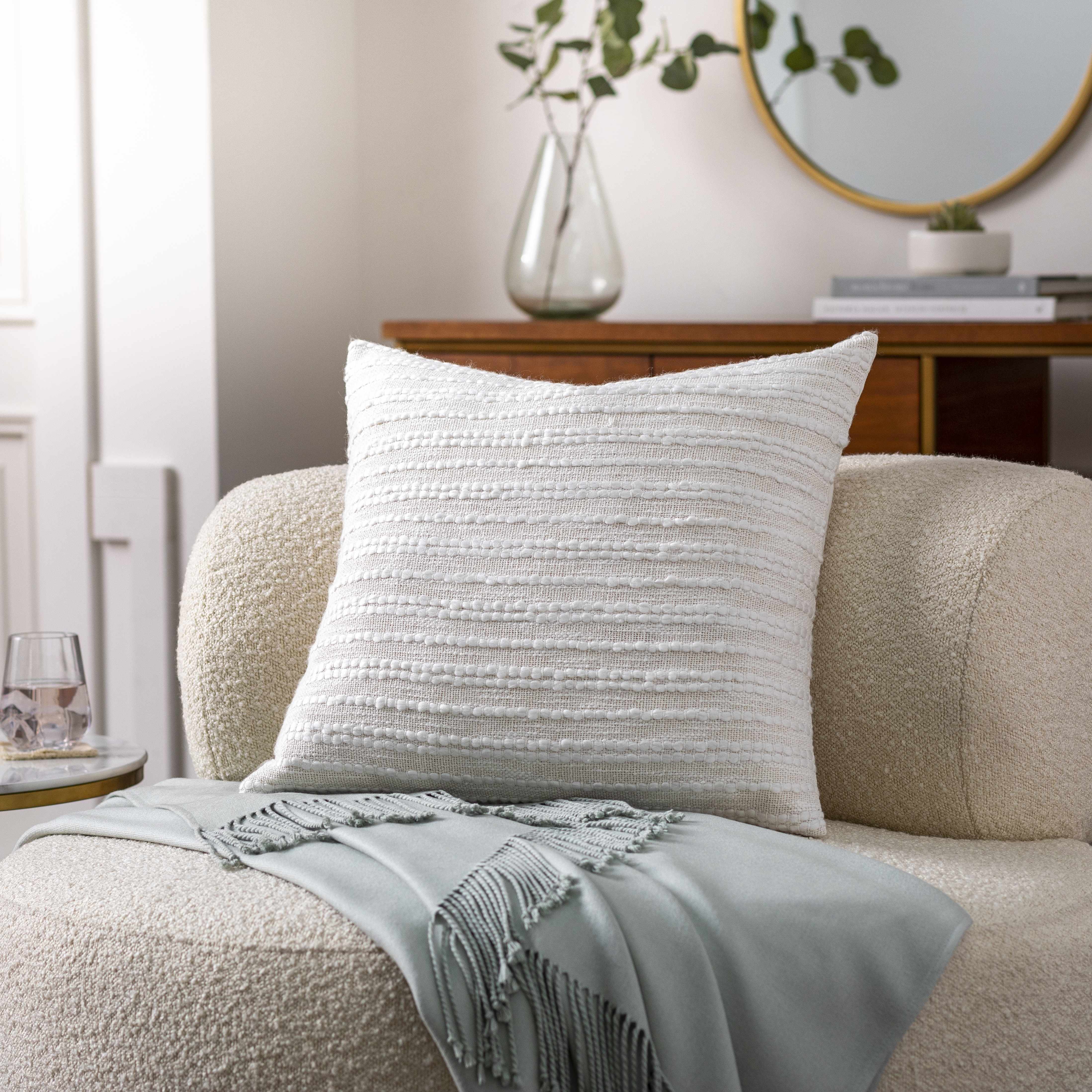 Textured throw pillow on a beige sofa with a light blue blanket and decorative items in the background.