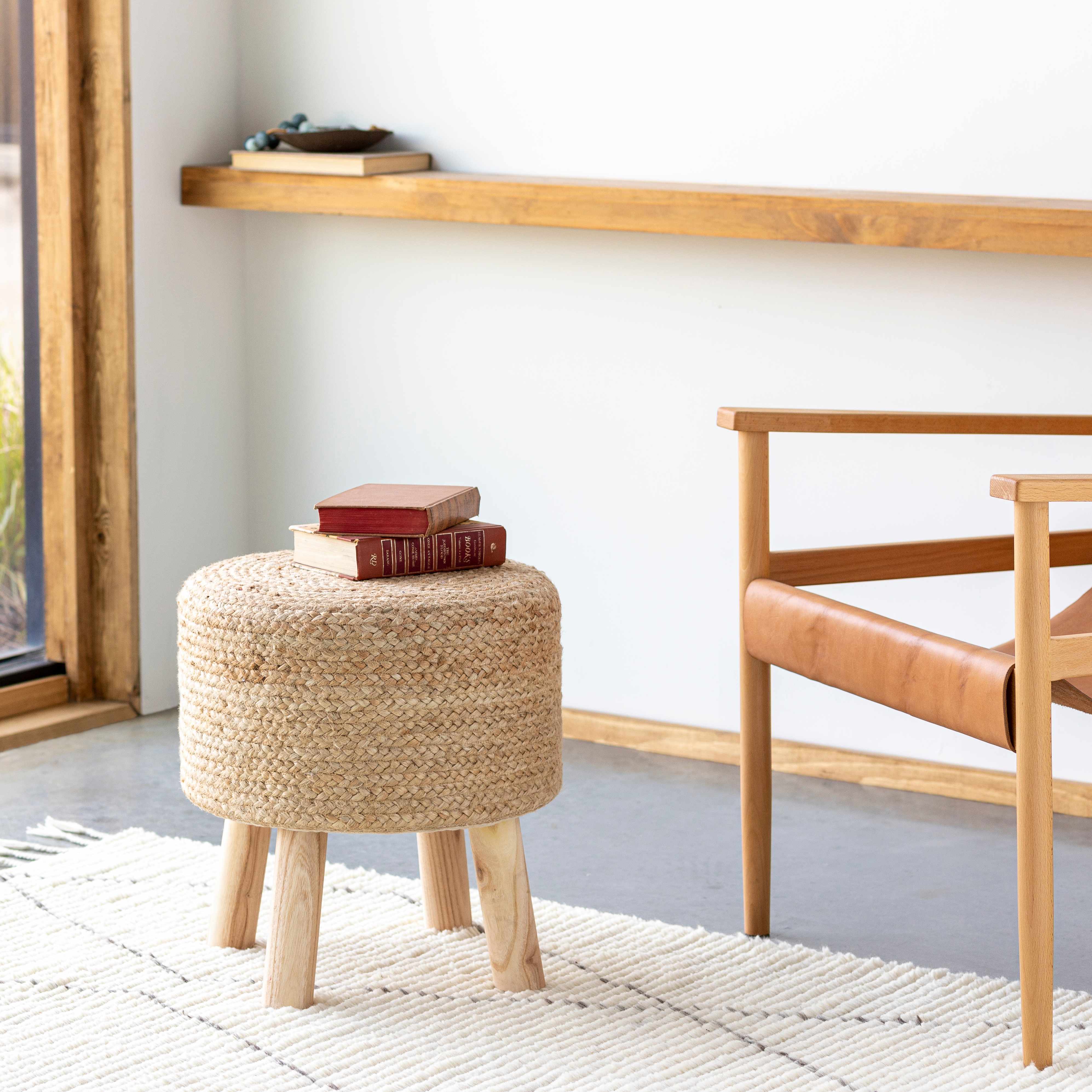 Woven stool with books on top in a room with a wooden shelf and chair.