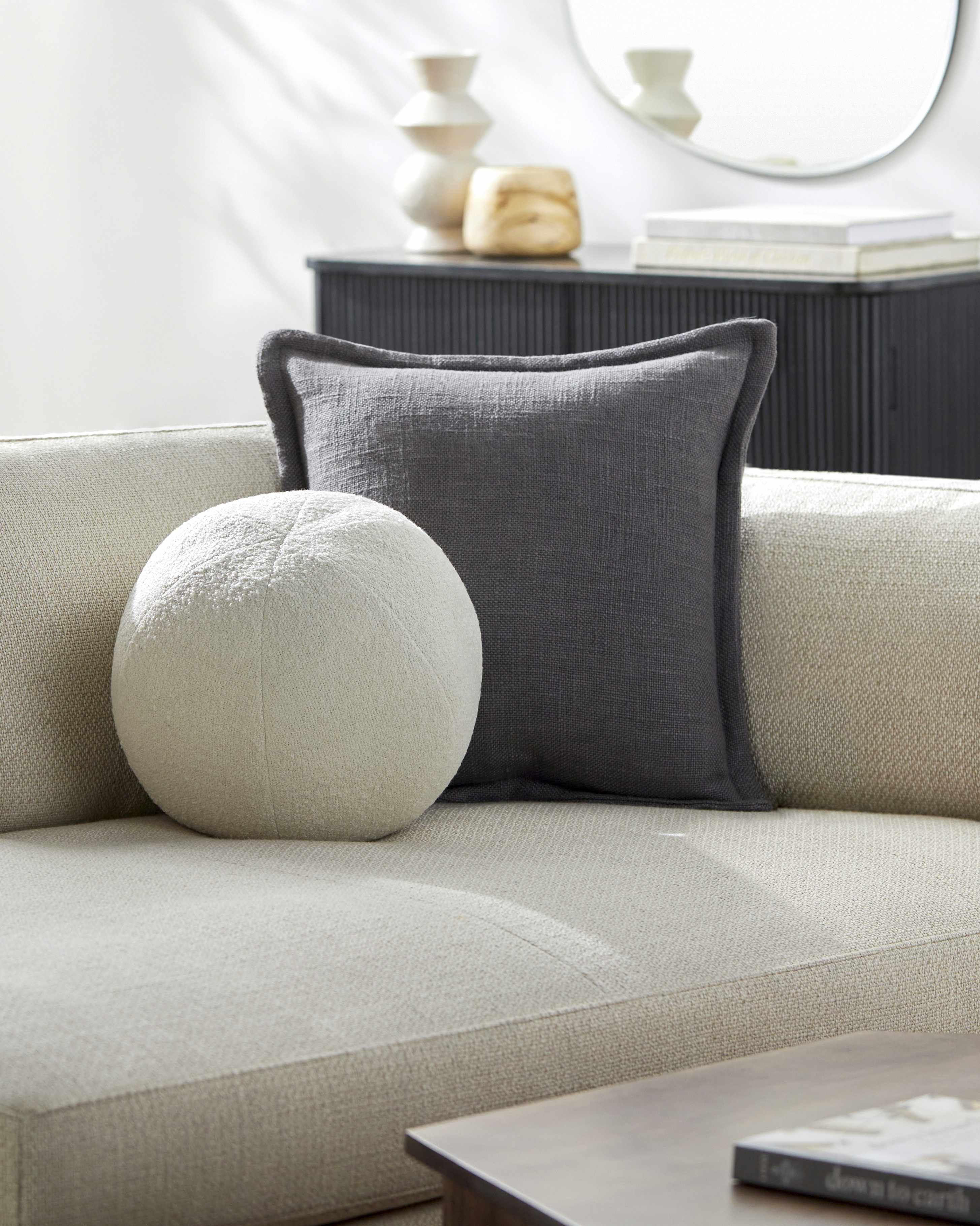 Gray pillow on a beige sofa with a white wall and decorative items in the background